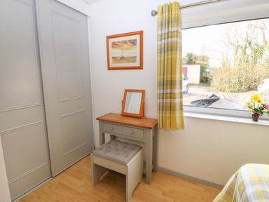 A dressing table with a mirror and cushioned stool next to a window with yellow plaid curtains at Plas Marchog Annexe in Rhoscefnhir near Pentraeth