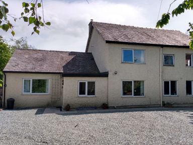 A two-story building with multiple windows and a gravel area in front at Plas Marchog Annexe in Rhoscefnhir near Pentraeth