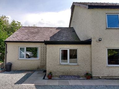 The exterior of a cream-colored building with a gravel and stone pathway and potted plants at Plas Marchog Annexe in Rhoscefnhir near Pentraeth