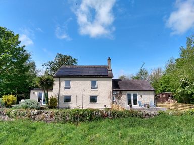 A house with solar panels on the roof surrounded by grass and trees at Plas Marchog Annexe in Rhoscefnhir near Pentraeth