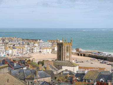 A coastal town with a stone church tower sandy beach boats and ocean in St Ives