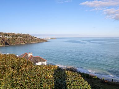 A coastal view with a house roof visible near the shore and a hill with trees in the background at Labour in Vain in St Ives