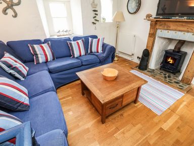 A living room with a blue sofa with striped cushions a wooden coffee table and a fireplace with a fire burning at Labour in Vain in St Ives
