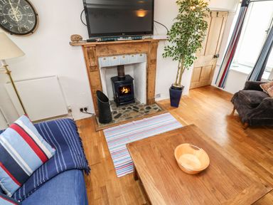 A living room with a wooden coffee table a blue sofa and a fireplace with a wood stove at Labour in Vain in St Ives