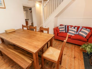 A dining area with a wooden table and chairs a red sofa with cushions under the stairs and a plant on the floor at Labour in Vain in St Ives