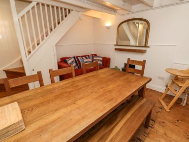 A dining room with a wooden table and chairs a red sofa under the stairs and a mirror on the wall at Labour in Vain St Ives