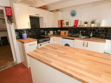 A kitchen with wooden countertops white cabinets a stove microwave washing machine and various kitchen items at Labour in Vain St Ives