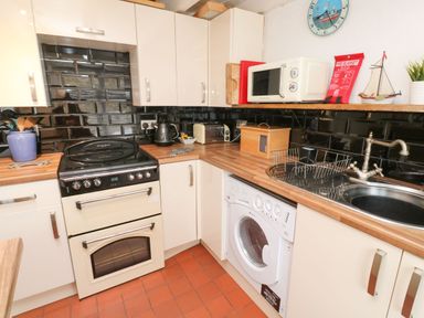 A kitchen with a stove, washing machine, microwave, kettle, toaster, sink, cupboards, and a wall clock at Labour in Vain in St Ives