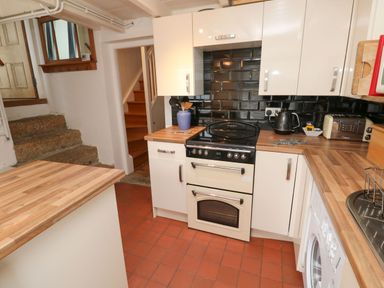 A kitchen with a stove cooker wooden countertops white cabinets a washing machine and steps leading to another room at Labour in Vain in St Ives