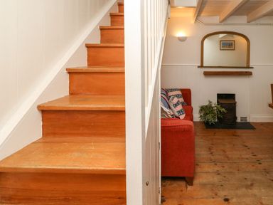 A wooden staircase next to a red sofa with patterned cushions and a small fireplace under a mirror at Labour in Vain in St Ives