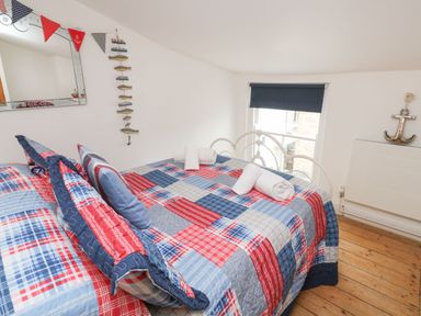 A bedroom with a double bed covered in a red blue and white patchwork quilt and rolled white towels on the bed at Labour in Vain in St Ives