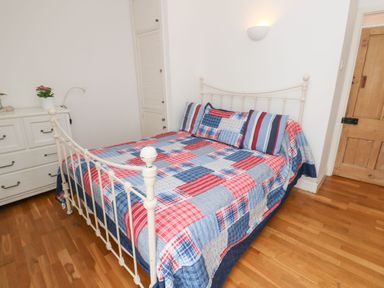 A bedroom with a metal bed frame a patterned bedspread a white dresser and a wooden door at Labour in Vain in St Ives