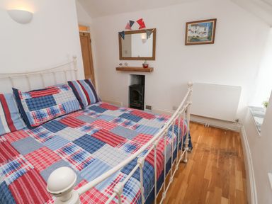 A bedroom with a white metal bed frame with red and blue patchwork bedding next to a small fireplace with a mirror above it at Labour in Vain in St Ives
