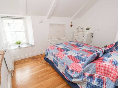 A bedroom with a bed covered with a red blue and white patchwork quilt a white dresser a window and hardwood floor at Labour in Vain in St Ives
