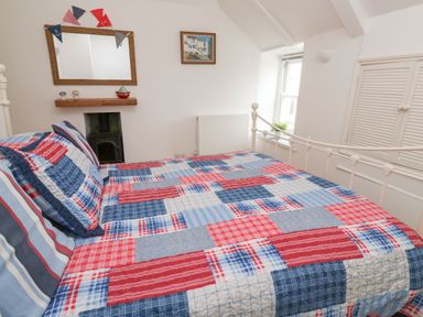 A bedroom with a bed covered in a red blue and white patchwork quilt and pillows under a window and a mirror at Labour in Vain in St Ives