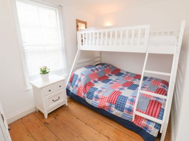 A bedroom with a white bunk bed with a patterned quilt and a white bedside table with a plant at Labour in Vain in St Ives