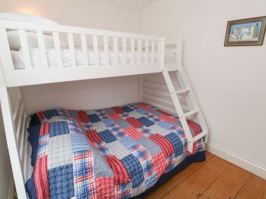 A bedroom with a white bunk bed and a quilted patchwork blanket on the bottom bed at Labour in Vain in St Ives