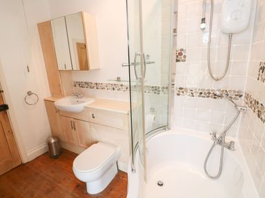 A bathroom with a bathtub shower combination toilet wooden floor and cabinets at Labour in Vain in St Ives
