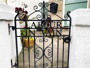 A black metal gate with the words Labour in Vain with plants and a green door behind at Labour in Vain in St Ives