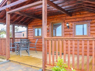 A wooden porch with a round table and four metal chairs at Alken Cabin in Bushmills County Antrim