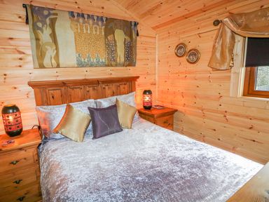 A bedroom with a wooden bed and side tables with lamps and a window at Alken Cabin in Bushmills County Antrim