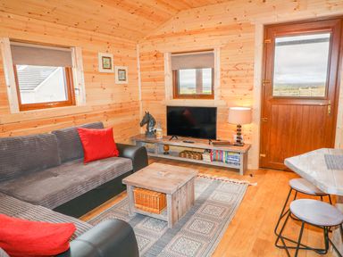 A living room with a sofa a wooden coffee table a TV on a stand and stools at Alken Cabin in Bushmills County Antrim