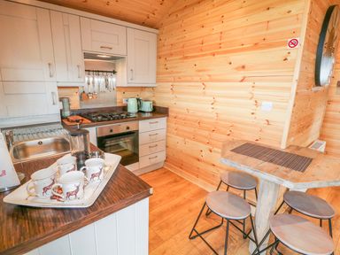 A kitchen with white cabinets a stove sink and a wooden table with stools at Alken Cabin in Bushmills County Antrim
