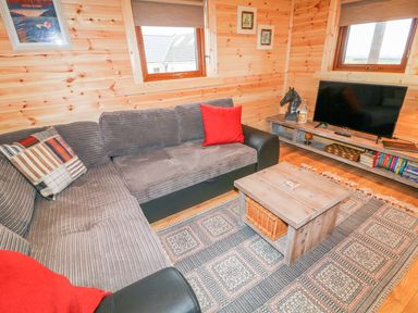 A living room with a gray sofa red cushions wooden coffee table and a television at Alken Cabin in Bushmills County Antrim