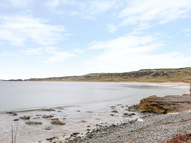 A rocky shoreline with a calm sea and distant green hills at Alken Cabin in Bushmills County Antrim