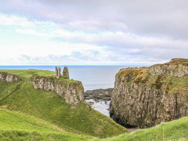 A coastal landscape with green cliffs and rocky ruins by the sea at Alken Cabin in Bushmills County Antrim
