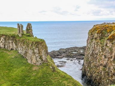 Coastal cliffs with ruins on the left cliff and rocky shore below at Alken Cabin in Bushmills County Antrim