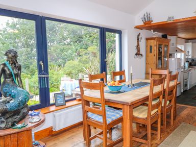 A dining area with wooden table and chairs next to blue framed windows and a mermaid statue at The Mermaid in Dungloe County Donegal