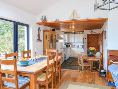 A dining area with a wooden table and chairs a kitchen with white cabinets and a wooden ceiling and a small round table with flowers at The Mermaid in Dungloe County Donegal