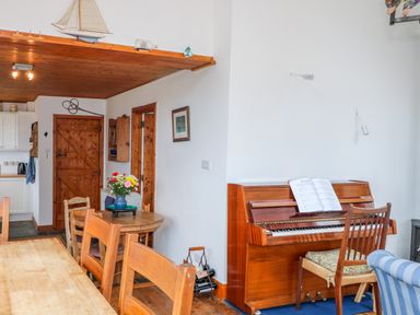 A dining area with wooden table and chairs flowers on a small table a piano with sheet music and a chair at The Mermaid in Dungloe County Donegal