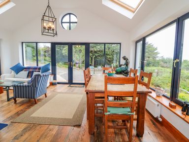 A dining area with a wooden table and chairs next to large windows and a sitting area with a sofa and armchair at The Mermaid in Dungloe County Donegal