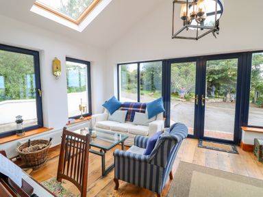 A sitting area with a white sofa and striped armchair around a glass coffee table near large windows and a skylight at The Mermaid in Dungloe County Donegal