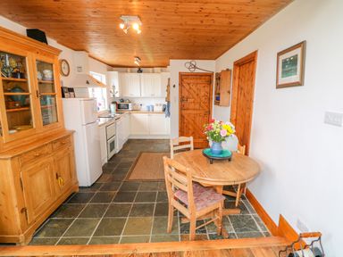 A kitchen and dining area with a wooden table and chairs a wooden cabinet white appliances and wooden ceiling at The Mermaid in Dungloe County Donegal