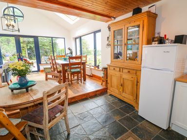 A kitchen dining area with wooden chairs tables a wooden cabinet and refrigerator at The Mermaid in Dungloe County Donegal