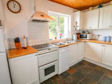 A kitchen with white cabinets a stove a dishwasher a microwave a sink and a window at The Mermaid in Dungloe County Donegal