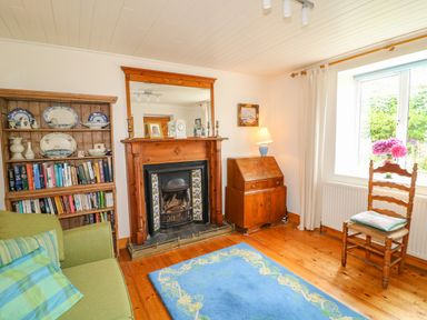 A sitting room with green sofa and bookshelf beside a wooden fireplace and a wooden chair near a window at The Mermaid in Dungloe County Donegal