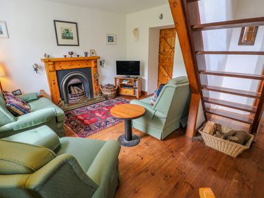 A living room with green armchairs a fireplace a wooden round table and a television at The Mermaid in Dungloe County Donegal