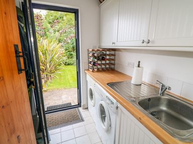 A utility room with a sink washing machine and dryer next to an open door leading to a garden at The Mermaid in Dungloe County Donegal