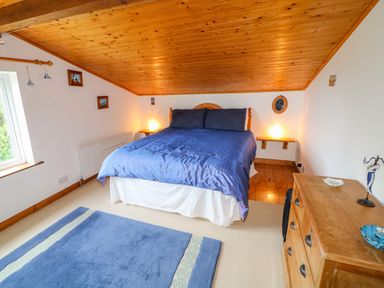 A bedroom with a blue bedspread wooden dresser blue rug and slanted wooden ceiling at The Mermaid in Dungloe County Donegal