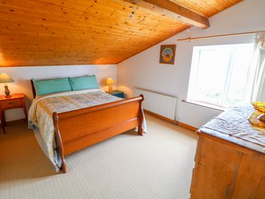 A bedroom with a wooden bed frame bedside tables with lamps a dresser and a window with a sloped wooden ceiling at The Mermaid in Dungloe County Donegal