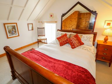 A bedroom with a wooden bed a large mirror a bedside table with a lamp a chair and framed pictures at The Mermaid in Dungloe County Donegal