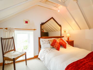 A bedroom with a bed with pillows and a red throw beside a wooden chair and a window at The Mermaid in Dungloe County Donegal