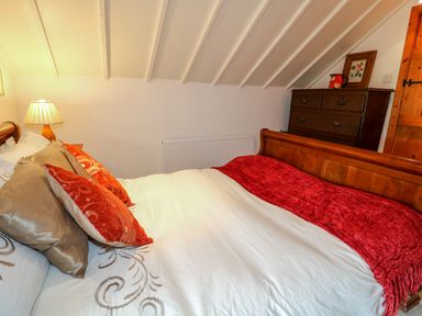 A bedroom with a bed with decorative pillows and a red throw next to a wooden dresser with a lamp at The Mermaid in Dungloe County Donegal