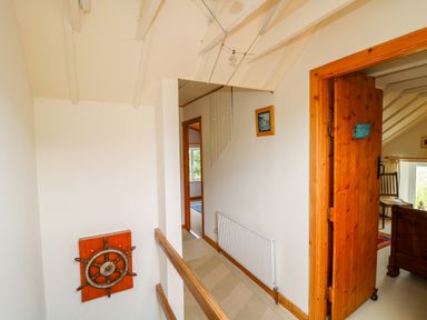 A hallway with a wooden ship wheel mounted on the wall and wooden door leading to a room at The Mermaid in Dungloe County Donegal