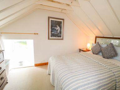 A bedroom with a bed with pillows and a striped blanket a bedside table with a lamp and a framed picture on the wall at The Mermaid in Dungloe County Donegal