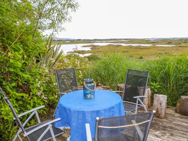 An outdoor seating area with four chairs around a table covered with a blue cloth and a lantern on the table overlooking greenery and water at The Mermaid in Dungloe County Donegal
